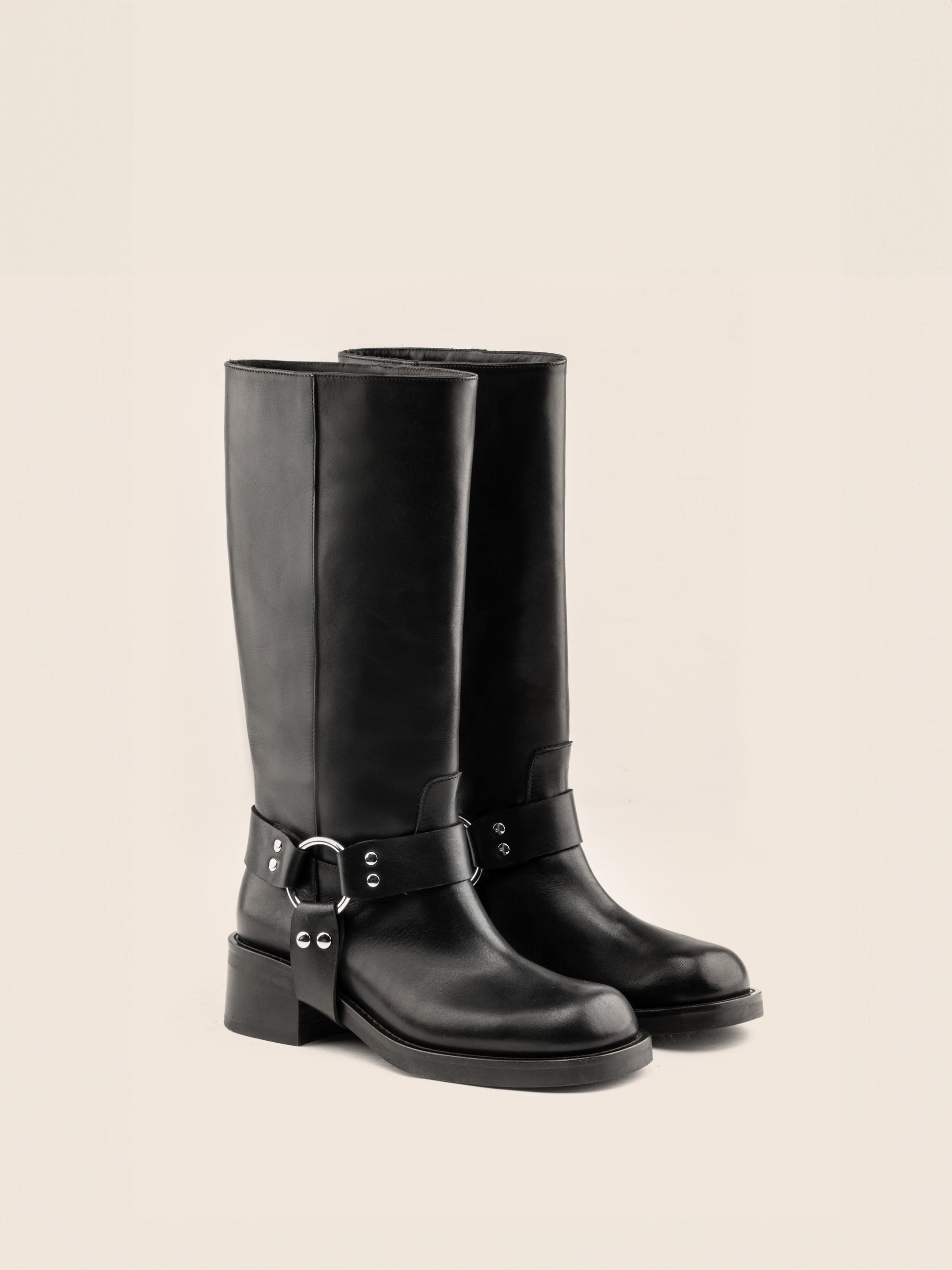 A black leather boot with a harness detail and block heel, on a white background.