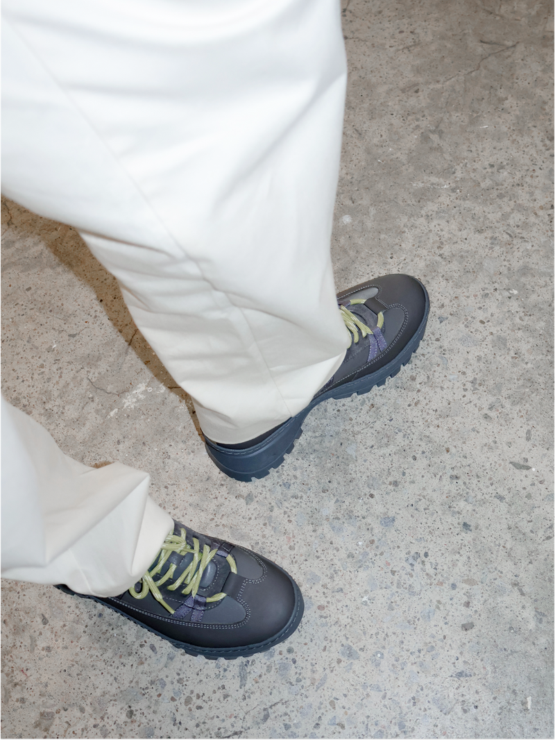 Person wearing grey shoes with yellow laces on a concrete floor