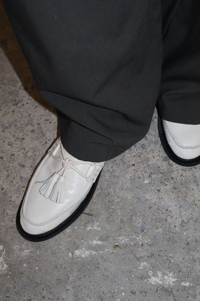 woman with gray pants wearing cream loafers with pompoms, on multicoloured gray floor
