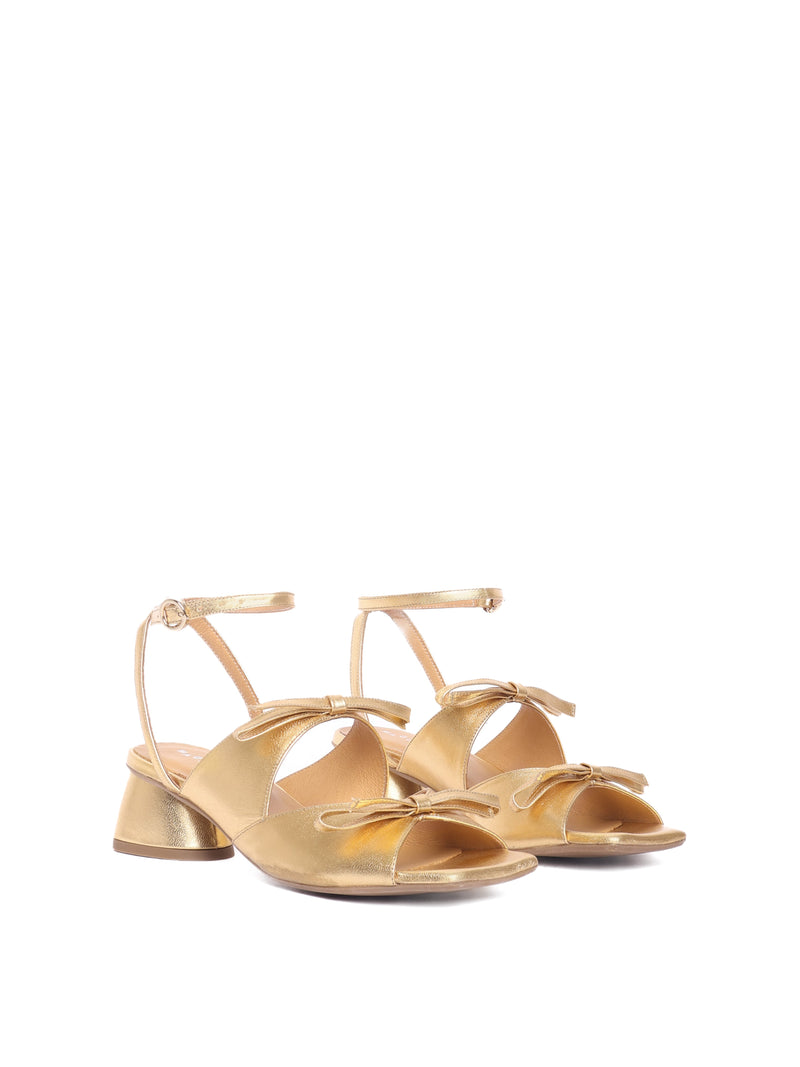 Gold leather heels with two straps adorned with bows and an ankle strap