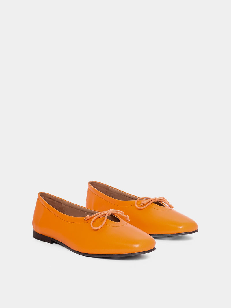Pair of orange shoes with bow details on a white background