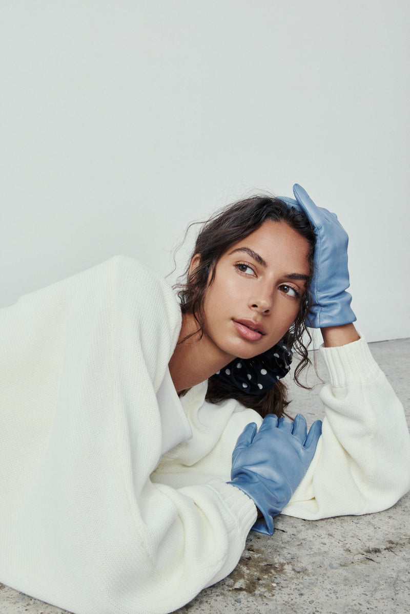 Person wearing a white sweater and blue gloves on a plain background