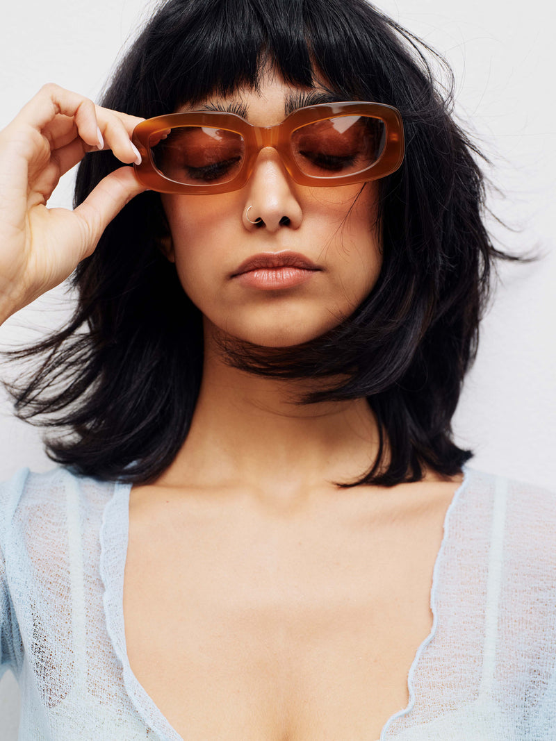 Brown hair model holding tan sunglasses in front or her eyes.