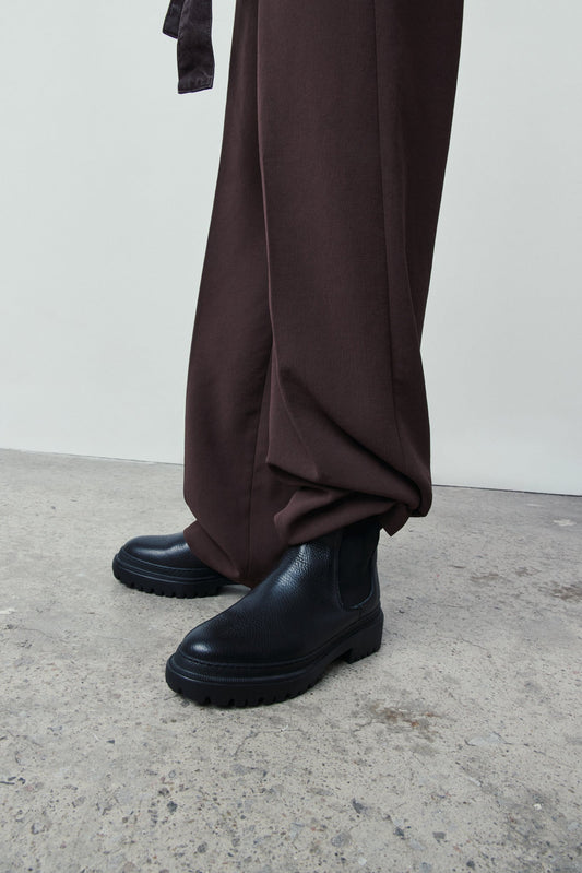 Black boots and brown pants on a plain background