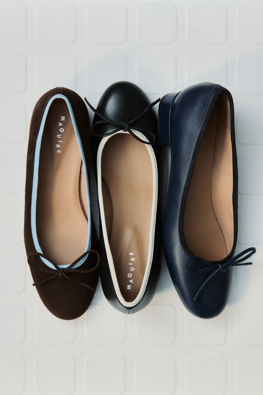 Three pairs of flats in brown, black, and navy on a light wooden surface.