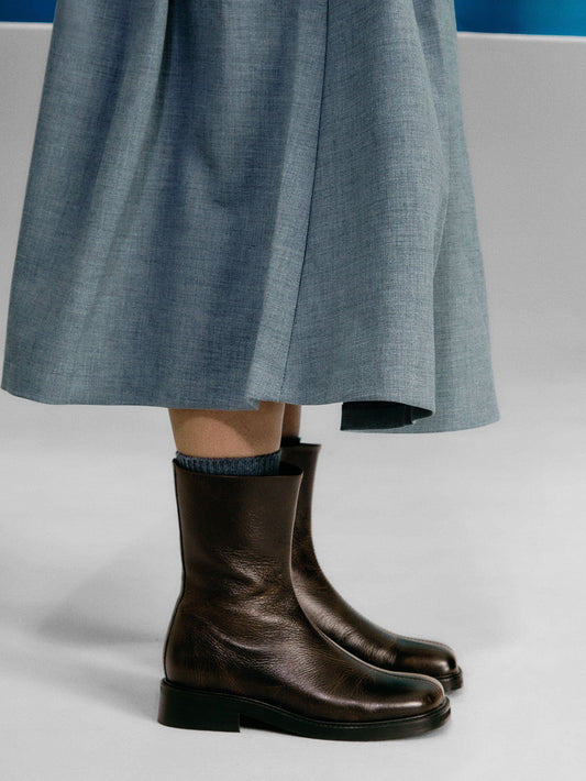 Brown boots worn with a light blue skirt on a neutral background