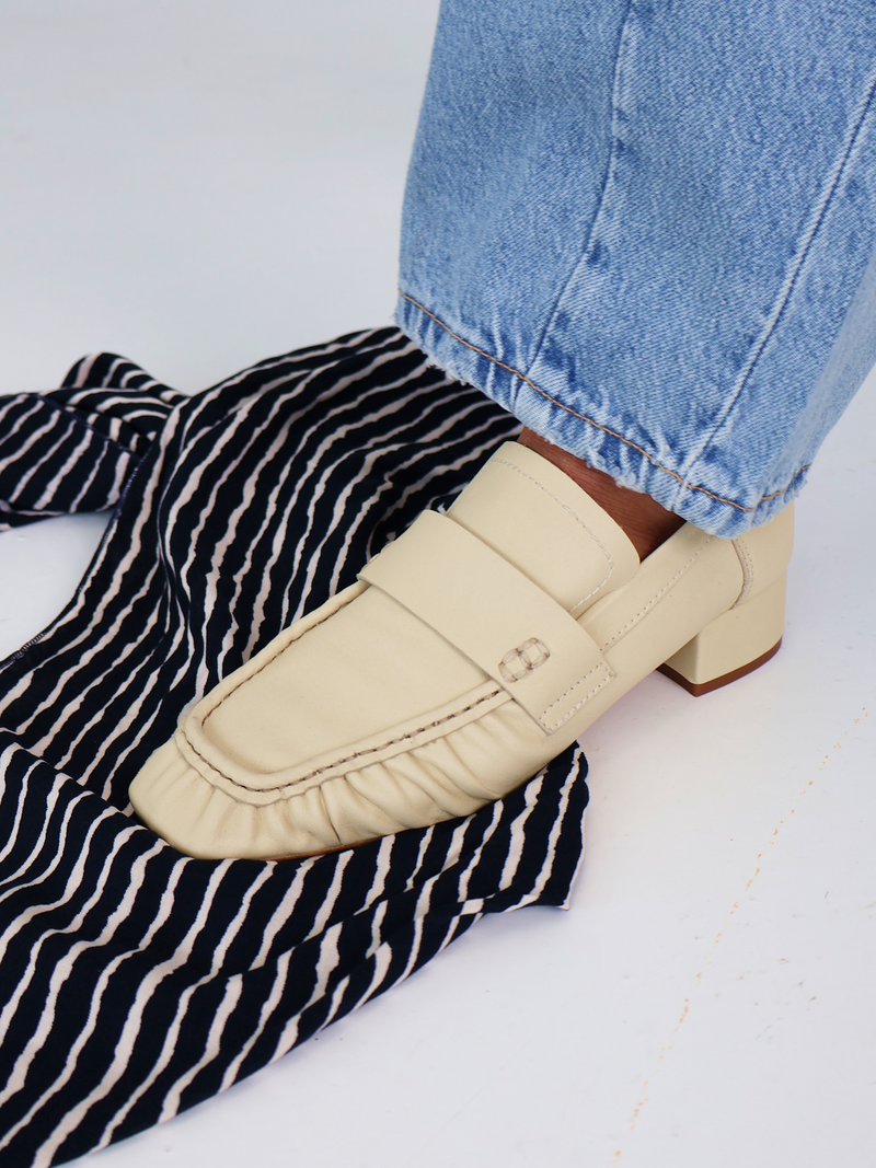 Light Yellow  loafers worn with black and white striped pants and blue jeans on a light background