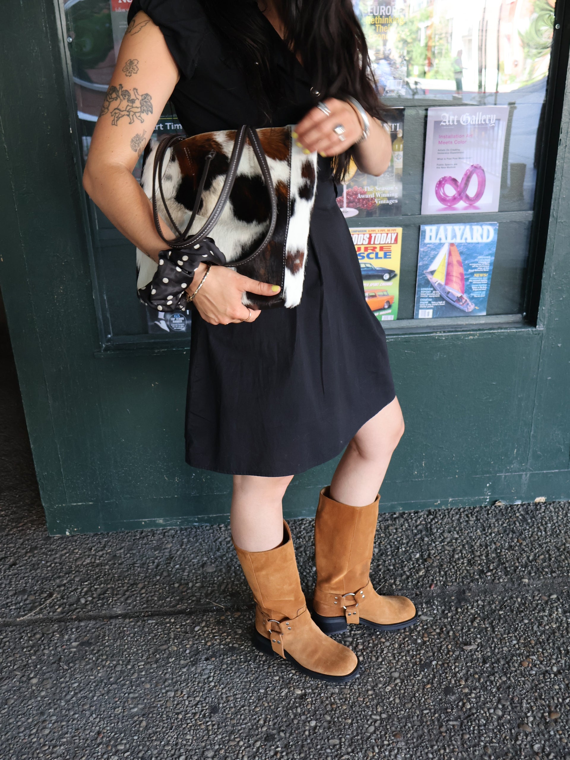 Person wearing  tan knee-high boots and a black dress leaning against a green wall.