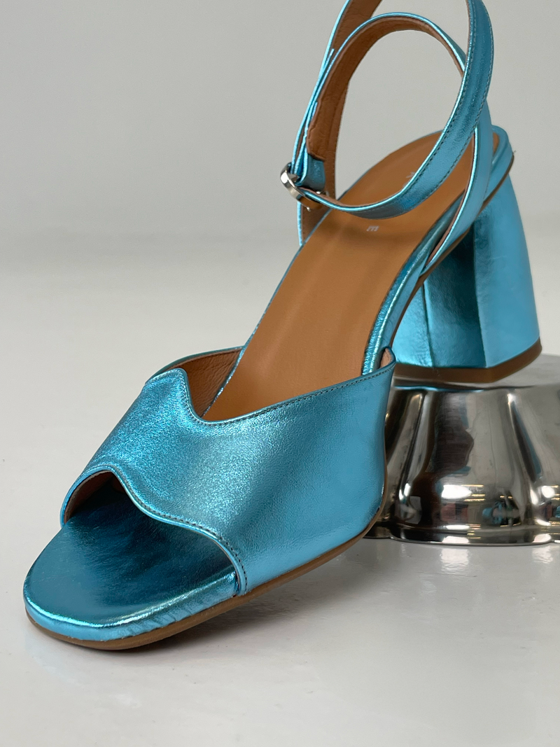 A blue metallic heel with an asymmetric wave design and an adjustable ankle strap.