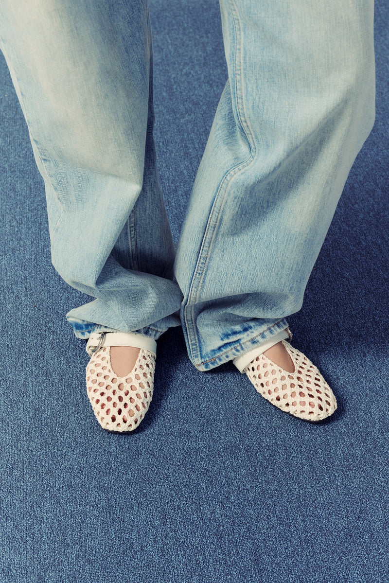 blue carpet, woman standing wearing light wash jeans and white leather woven mary jane ballet flats.