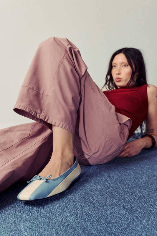 woman laying on blue carpet against white background, wearing dusty pink ants and red tank top with striped blue and white ballet flats.