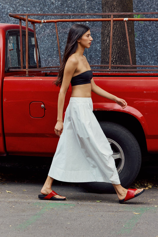 Woman wearing red sandals and a white dress walking in front of a red truck