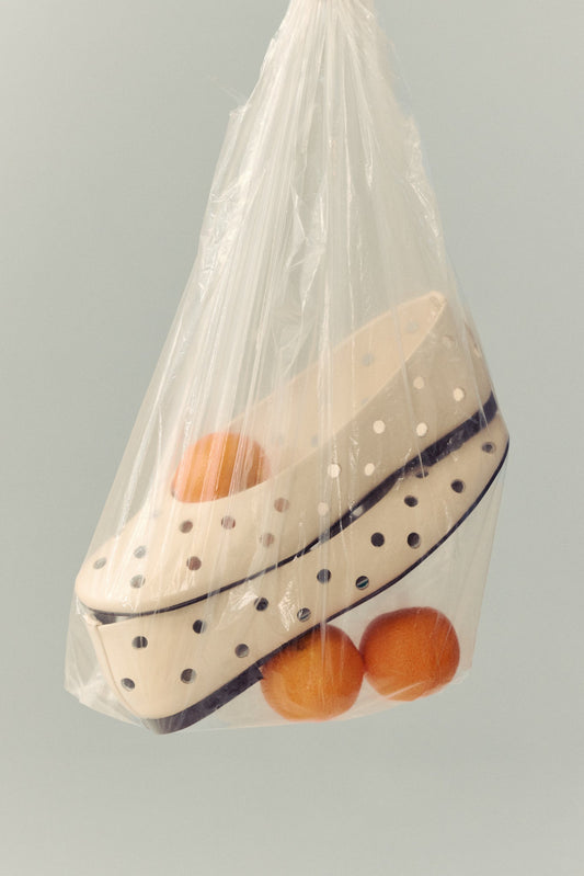 cream ballet flat with round cut outs in clear plastic blag with three clementines on white background
