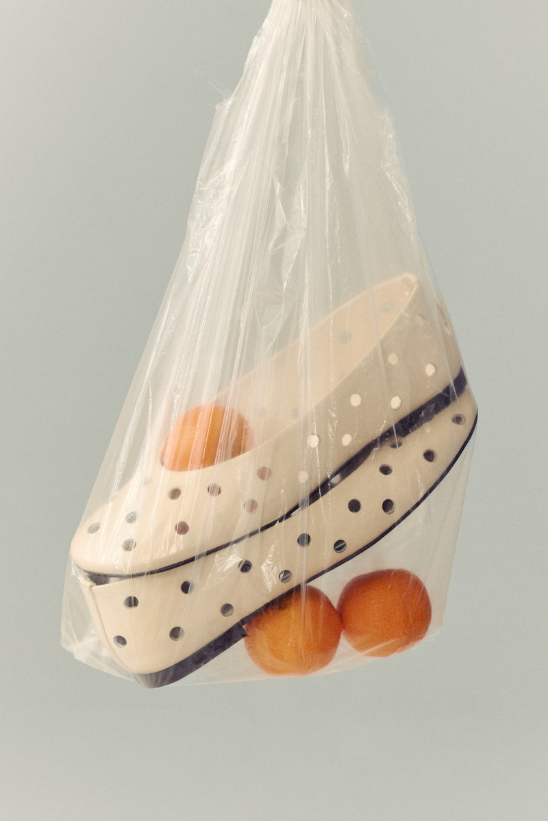 cream ballet flat with round cut outs in clear plastic blag with three clementines on white background
