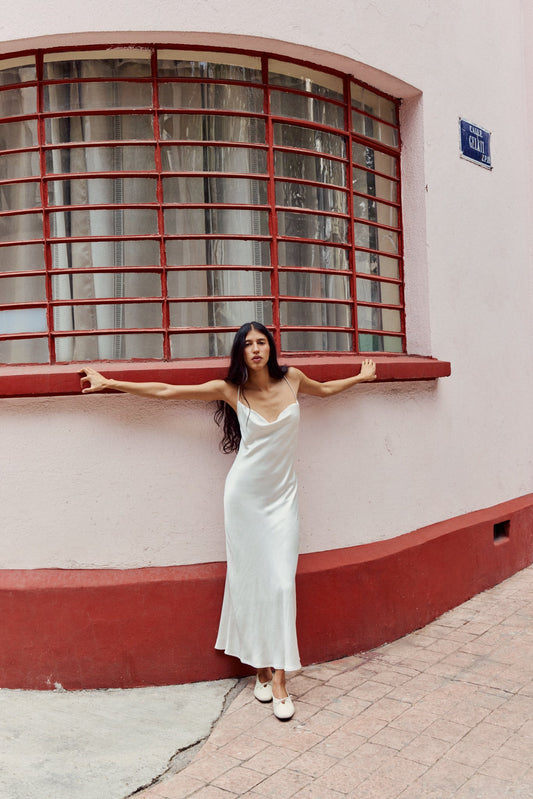 Woman wearing white dress with white ballet flats in front of colourful building
