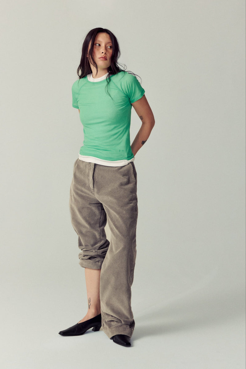 girl wearing corduroy taupe pants, green shirt and black heels in white studio