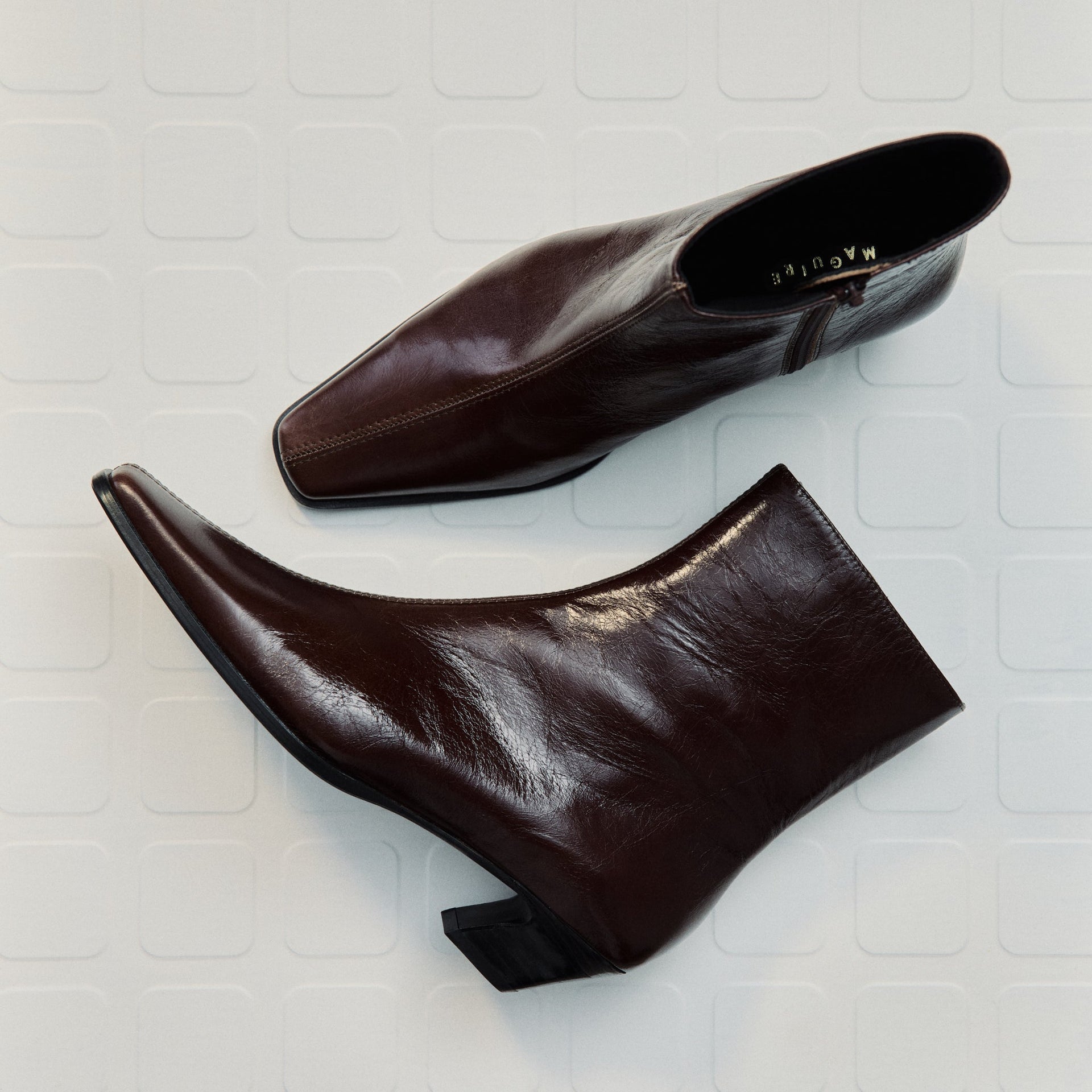 Pair of shinny brown leather ankle boots on a light gray tiled background