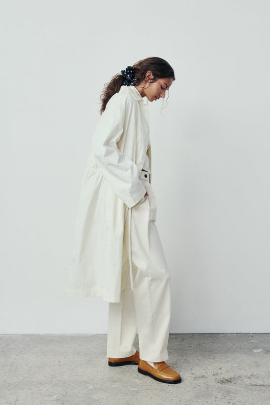 Person wearing a white coat and pants with tan shoes against a plain background