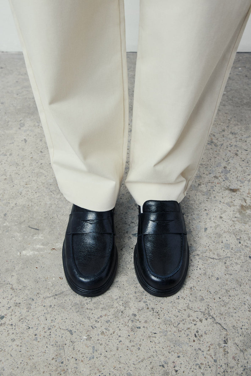 Person wearing black loafers and white pants on a concrete floor