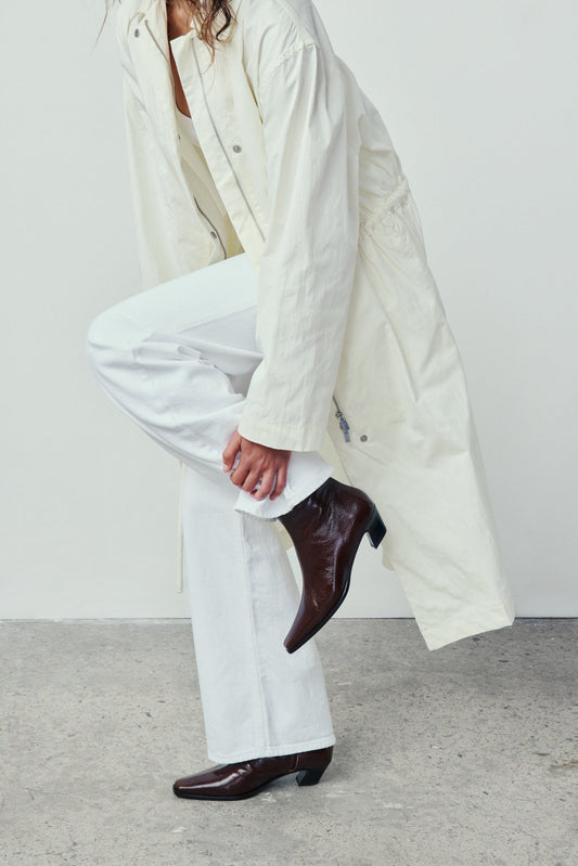 Person wearing a long white coat, white pants, and brown shoes on a plain background