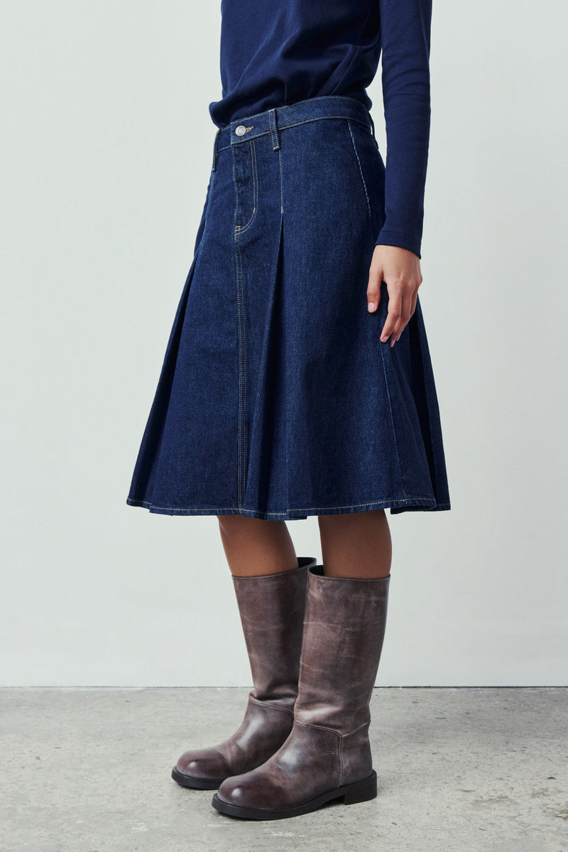 Person wearing a blue denim skirt and brown boots on a light gray background