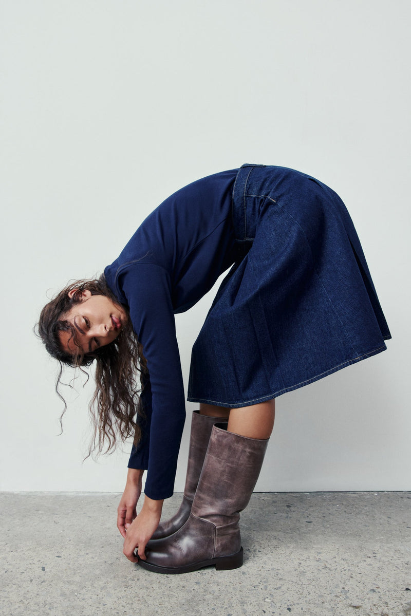 Person wearing a blue dress and brown boots against a plain background