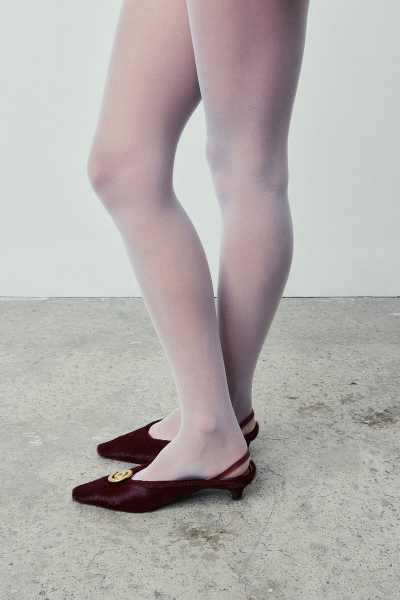 Person wearing sheer tights and Bordeaux shoes on a light background