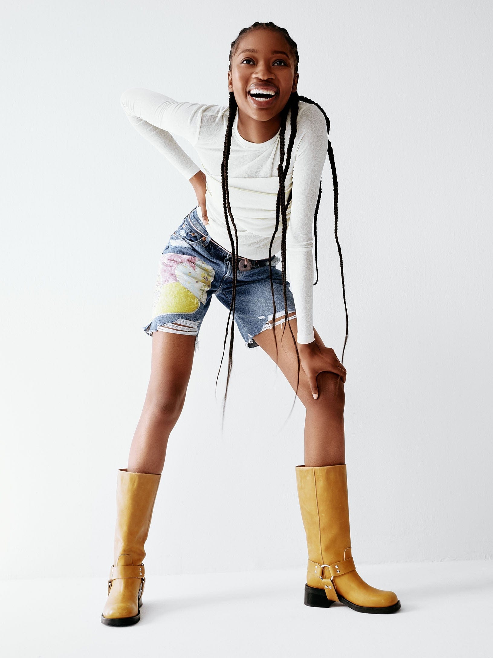A yellow tan leather boot with a harness detail and low heel worn by a model wearing short.