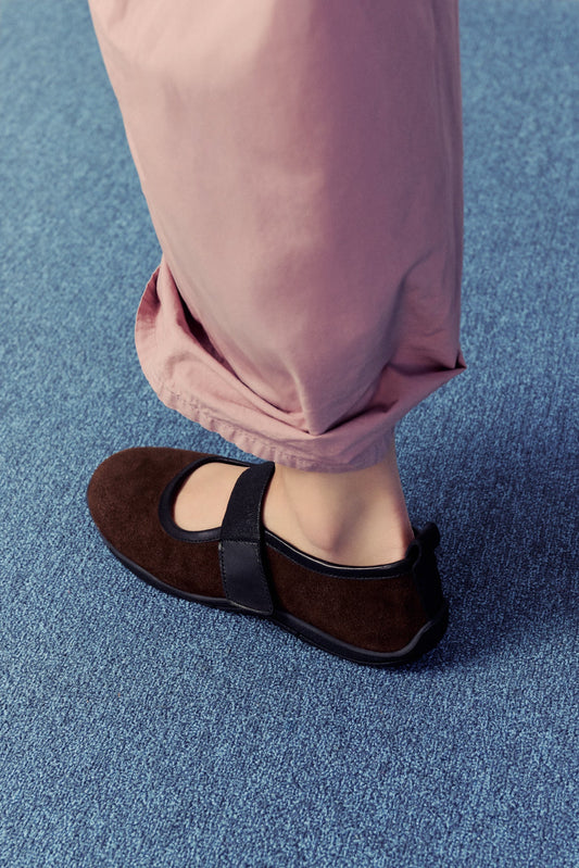 bottom half of a half, woman wearing dusty pink pants with brown flats on blue carpet.