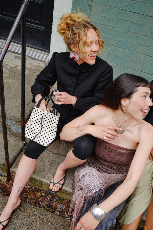 Two women sitting on a step, one holding a polka dot handbag.
