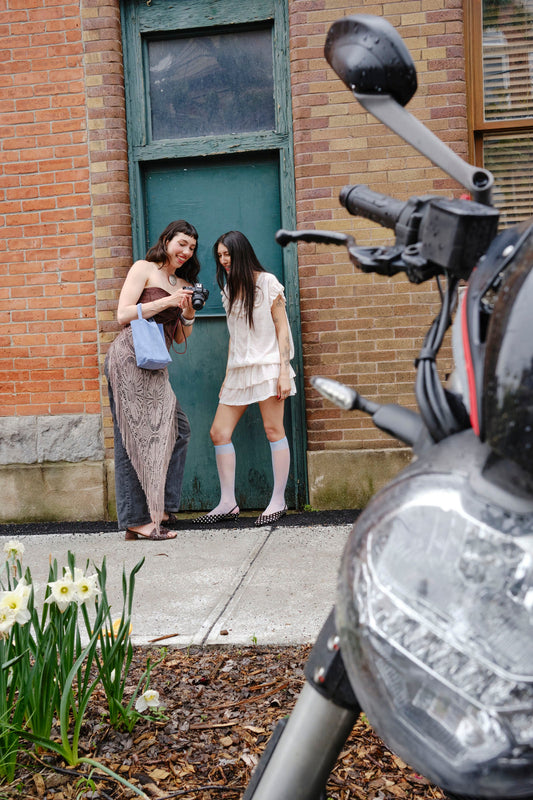 Two women standing next to a motorcycle with a brick building in the background
