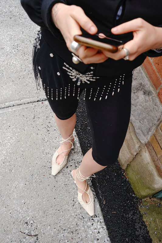 Overhead photo of a woman on her phone wearing a black outfit and white strap heels
