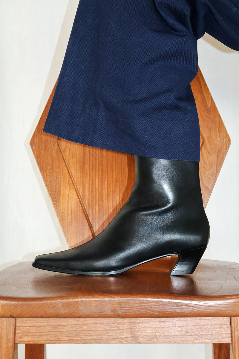Black ankle boots worn with a navy blue outfit on a wooden chair.