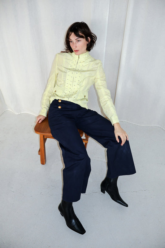 Woman sitting on a stool wearing a light green sweater and dark blue pants against a white background