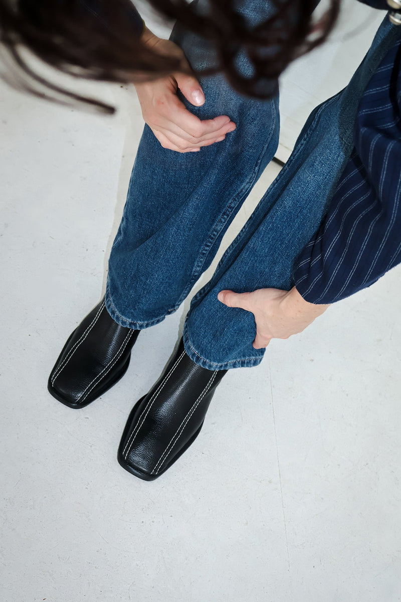 Woman bending down wearing jeans and black leather boots, hands on her knees and hair gracefully falling down.