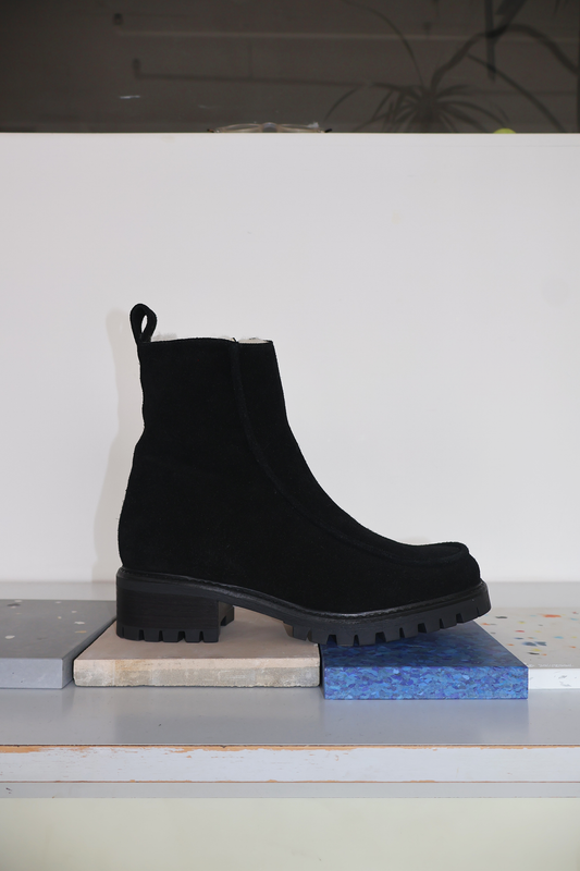 Shearling lined winter boot with a front piping detail, in a black suede with a black lug outsole. 