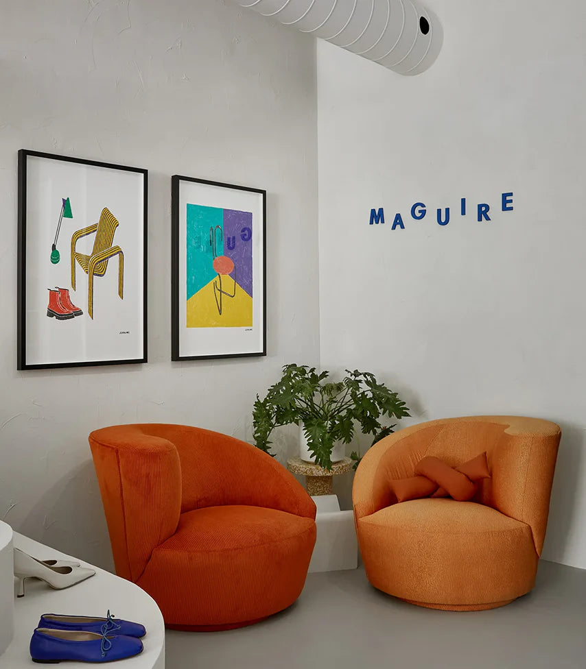 A cozy corner of our Toronto store featuring two vibrant orange sofas, the blue Maguire logo, and curated artwork on the walls.