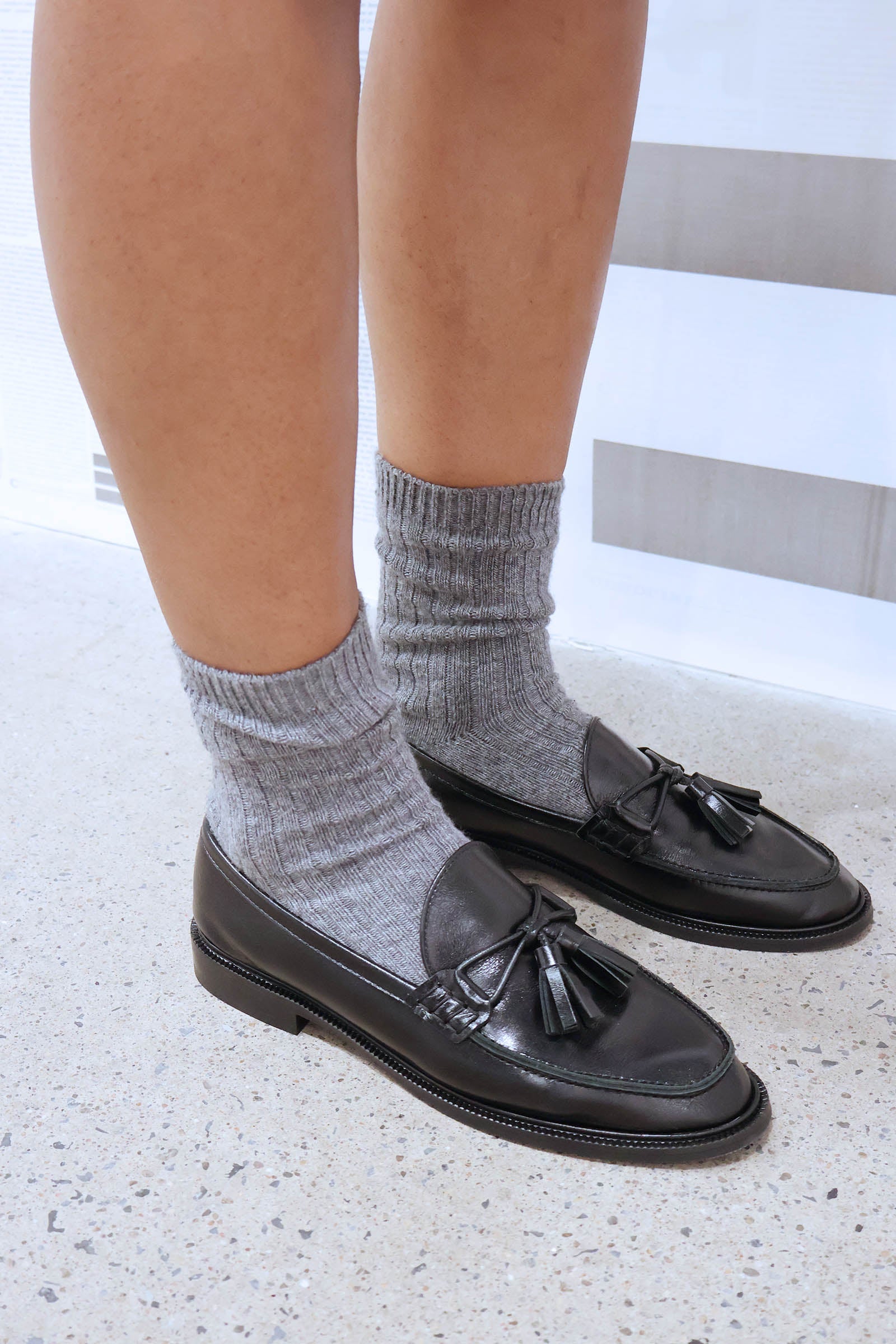 Black loafers with tassels worn with gray socks on a light background