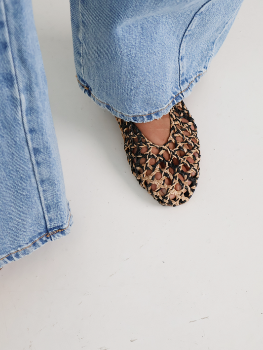 Natural woven ballerina flat with Mary-Jane strap worn with blue jeans on a white floor.