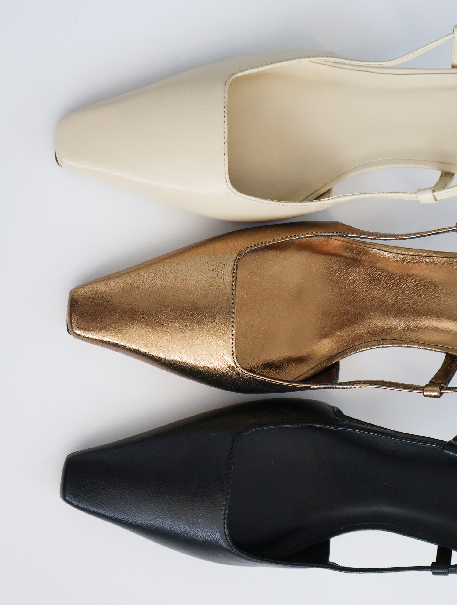 Three pairs of high-heeled shoes in beige, gold, and black on a light gray background.