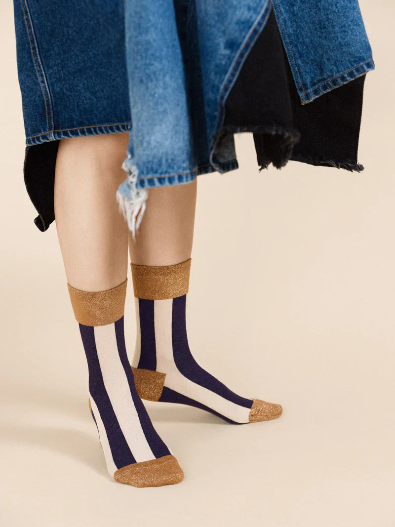 Black and white stripe sock with a gold edge. The model is wearing it with a sandal and a denim dress.