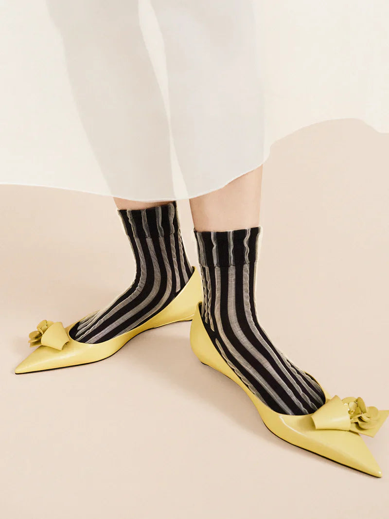 A pair of black and white striped socks worn with white pants and yellow pointed-toe heels.