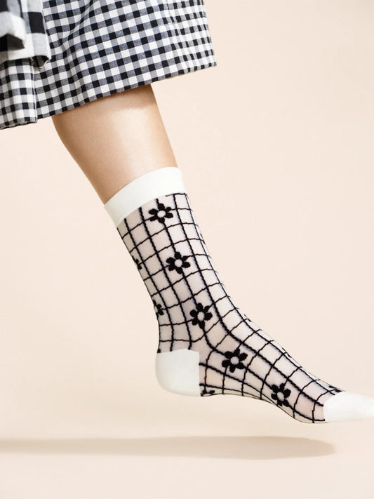 A pair of beige and black checkered socks with a floral pattern, worn with a black and white dress