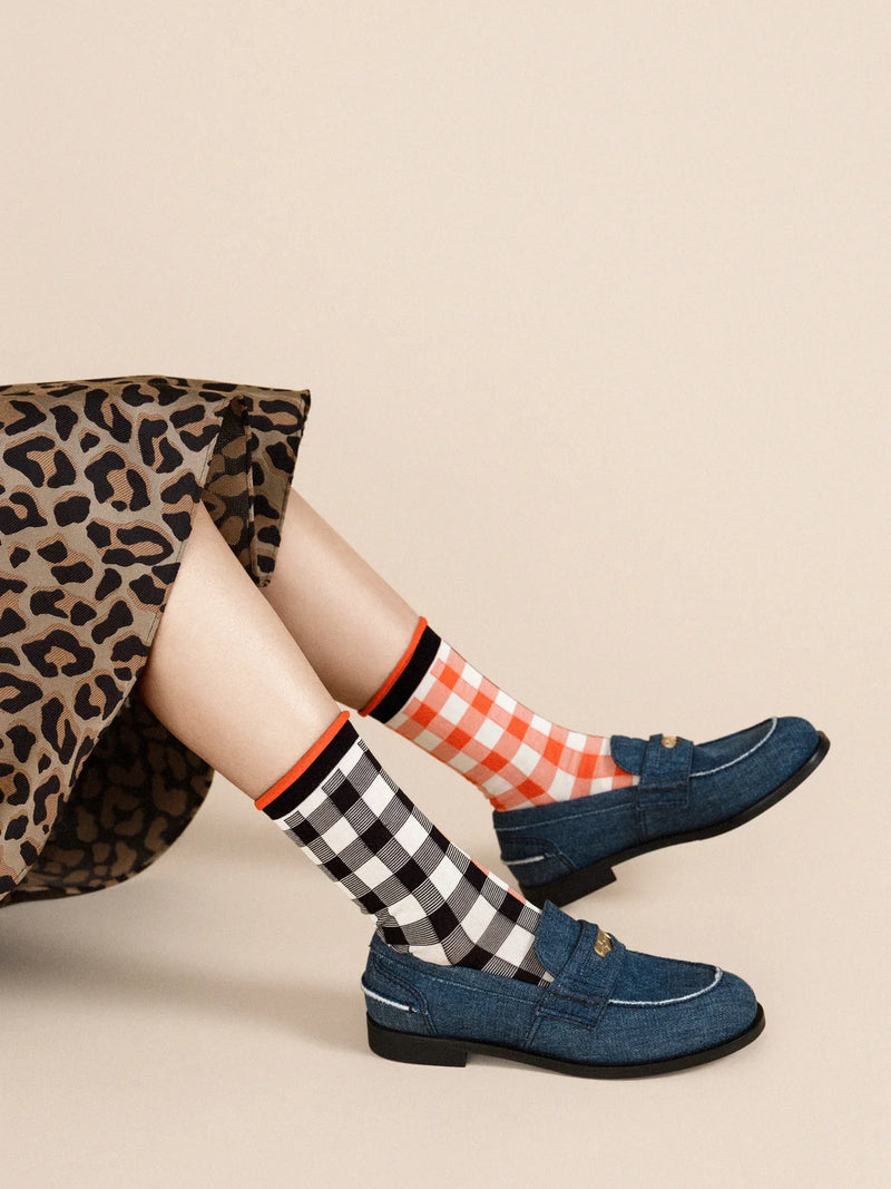 A pair of checkered socks in black, white, and red worn with blue loafers and a leopard print skirt.