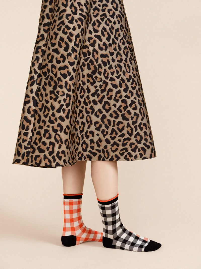 A pair of checkered socks in black, white, and red worn with a leopard print skirt.