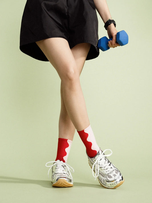 A person wearing silver sneakers and red and pink patterned socks standing on a green surface.