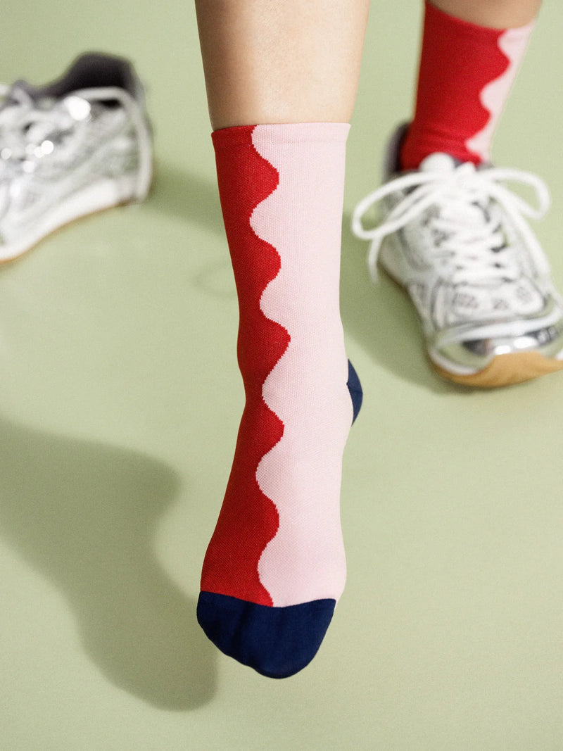A person wearing silver sneakers and red and pink patterned socks standing on a green surface.