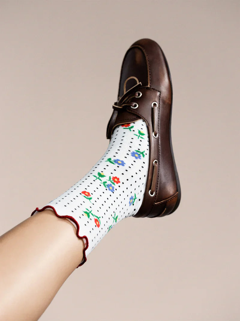 Brown leather shoe with a white sock featuring colorful floral patterns on a beige background
