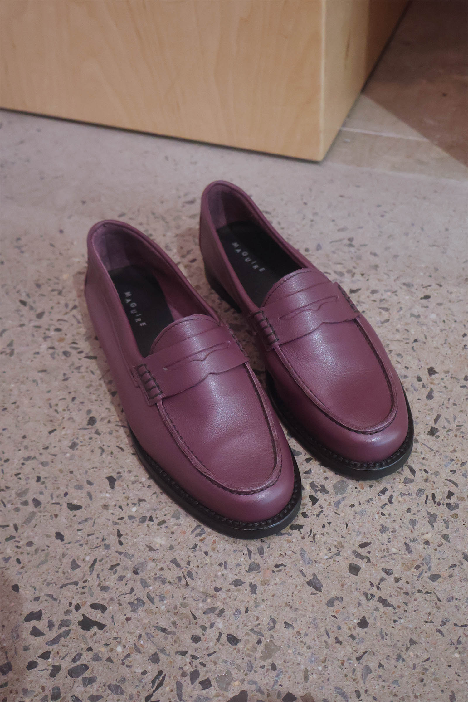 Pair of maroon loafers on a speckled floor.