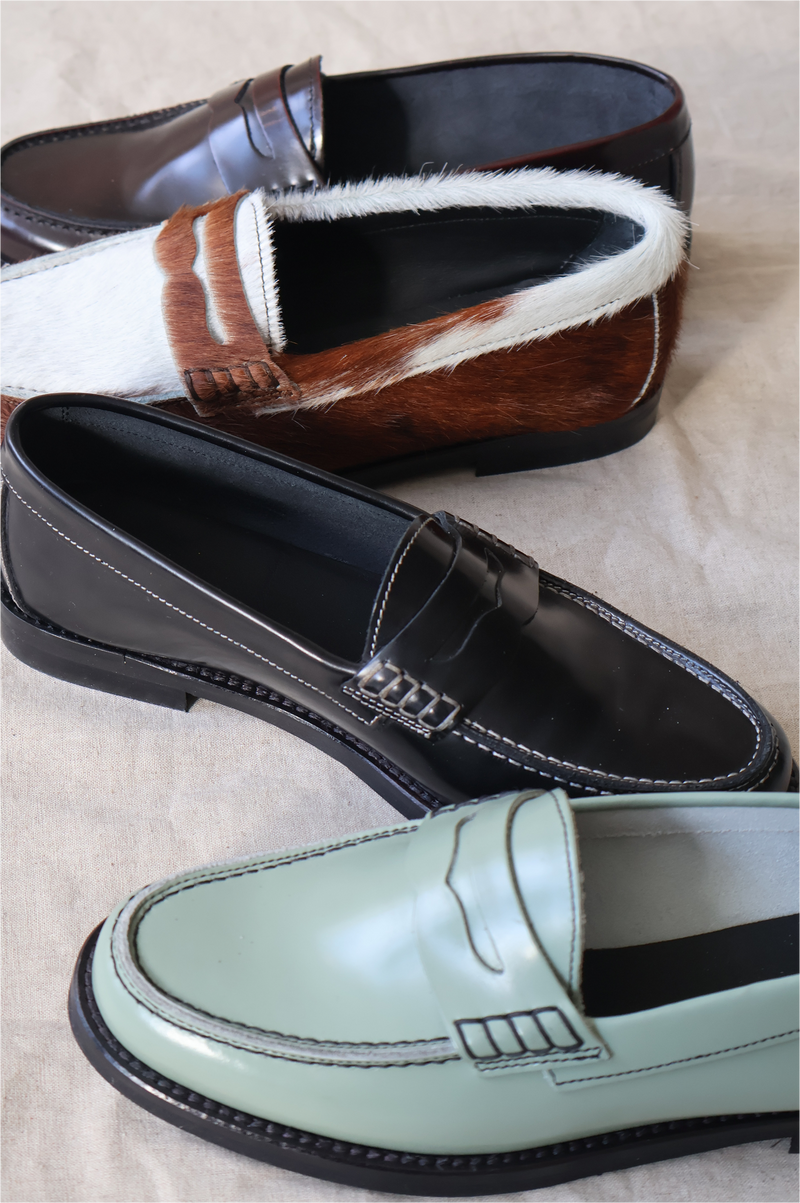 Four different styles of loafers on a neutral background